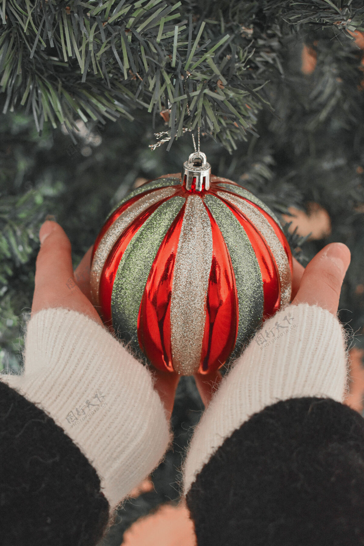 季节性一个人的手拿着一个漂亮的圣诞树上有红色和金色条纹的圣诞饰品灯新的礼物