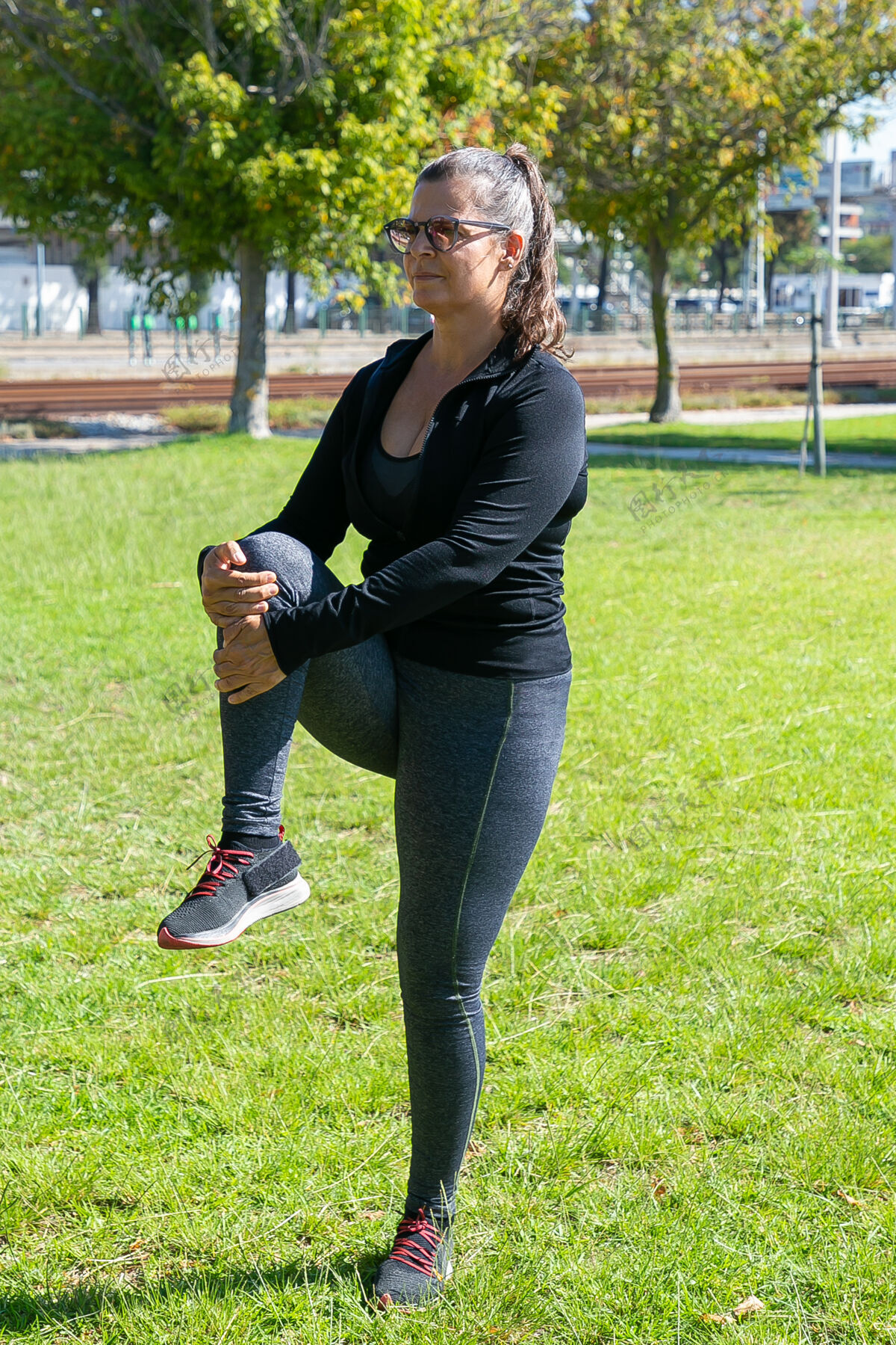 中年人专注于穿着健身服的成熟女性在公园草地上做早操 站立和伸展双腿健康或积极的生活方式概念慢跑者运动腿部