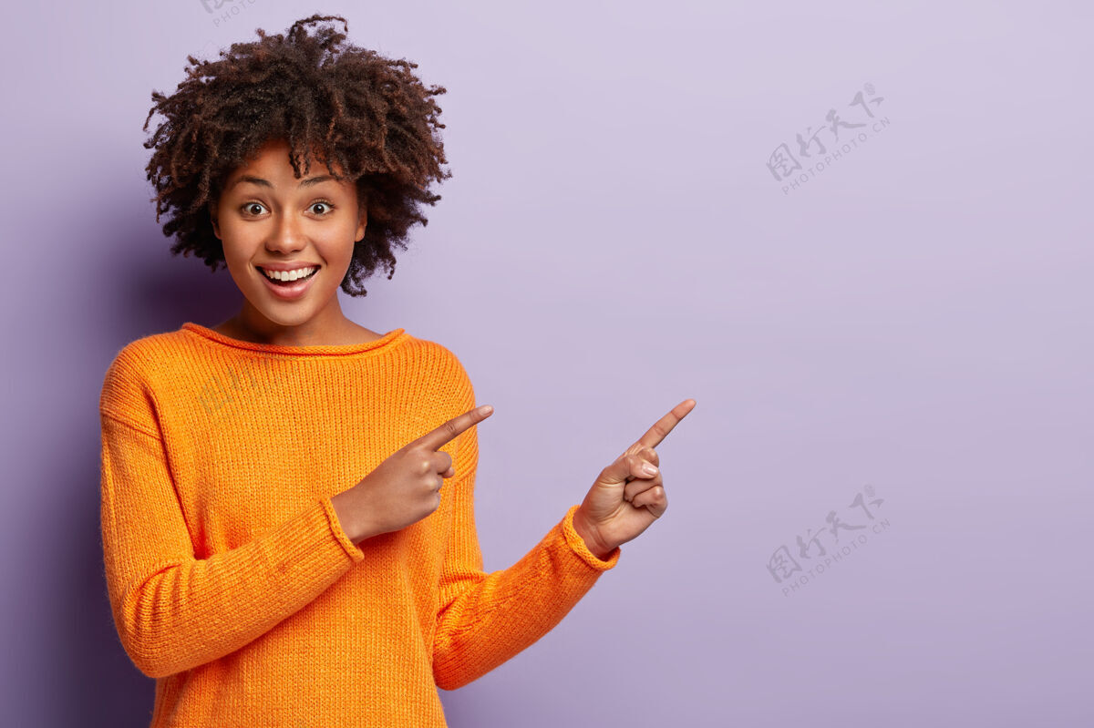 发型照片中的非洲裔美国妇女高兴地用食指指向远处 促销真棒的地方为您的广告内容个性现代手势