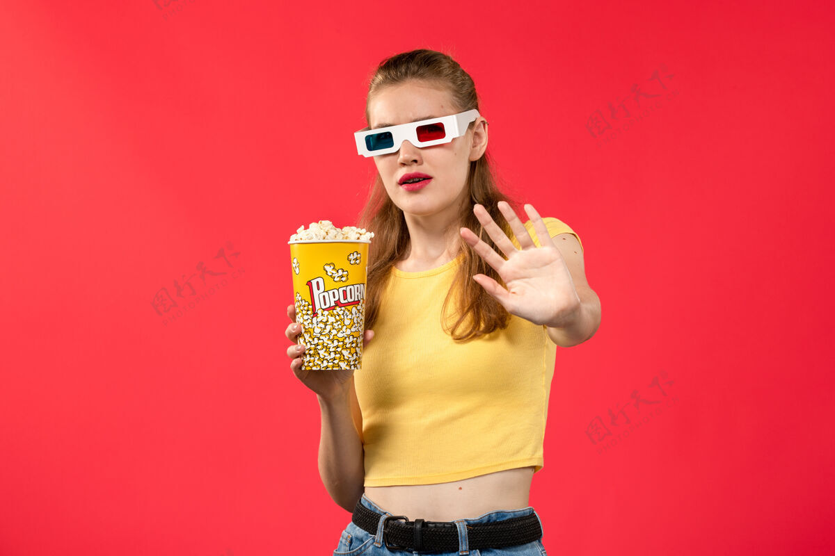 电影正面图年轻女性在电影院拿着爆米花包在红墙电影院看小吃好玩的电影电影院肖像年轻人