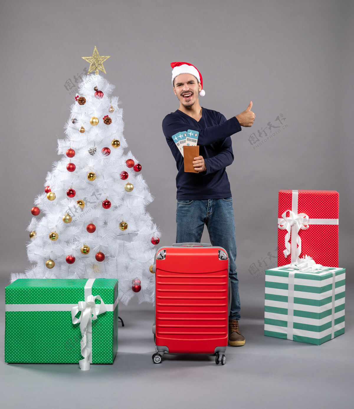 男人带着红色手提箱的笑脸男人拿着他的旅行票 向灰色竖起大拇指包手提箱圣诞老人