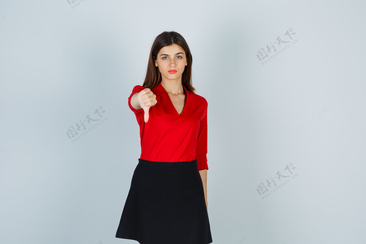 女人一个穿着红衬衫 黑裙子 大拇指朝下的年轻女人 看上去很不高兴向下表现成人