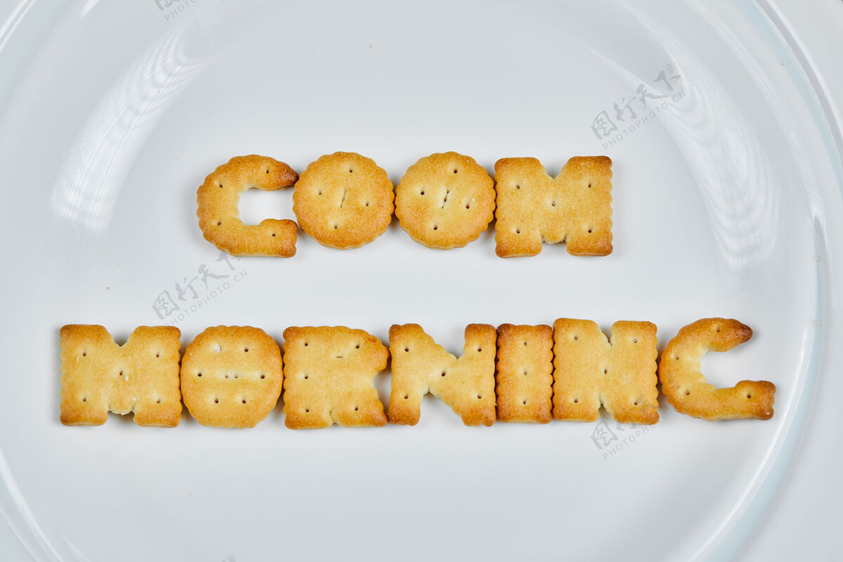 美味“早上好”这个词是用白色盘子上的饼干拼成的顶部视图小吃特写