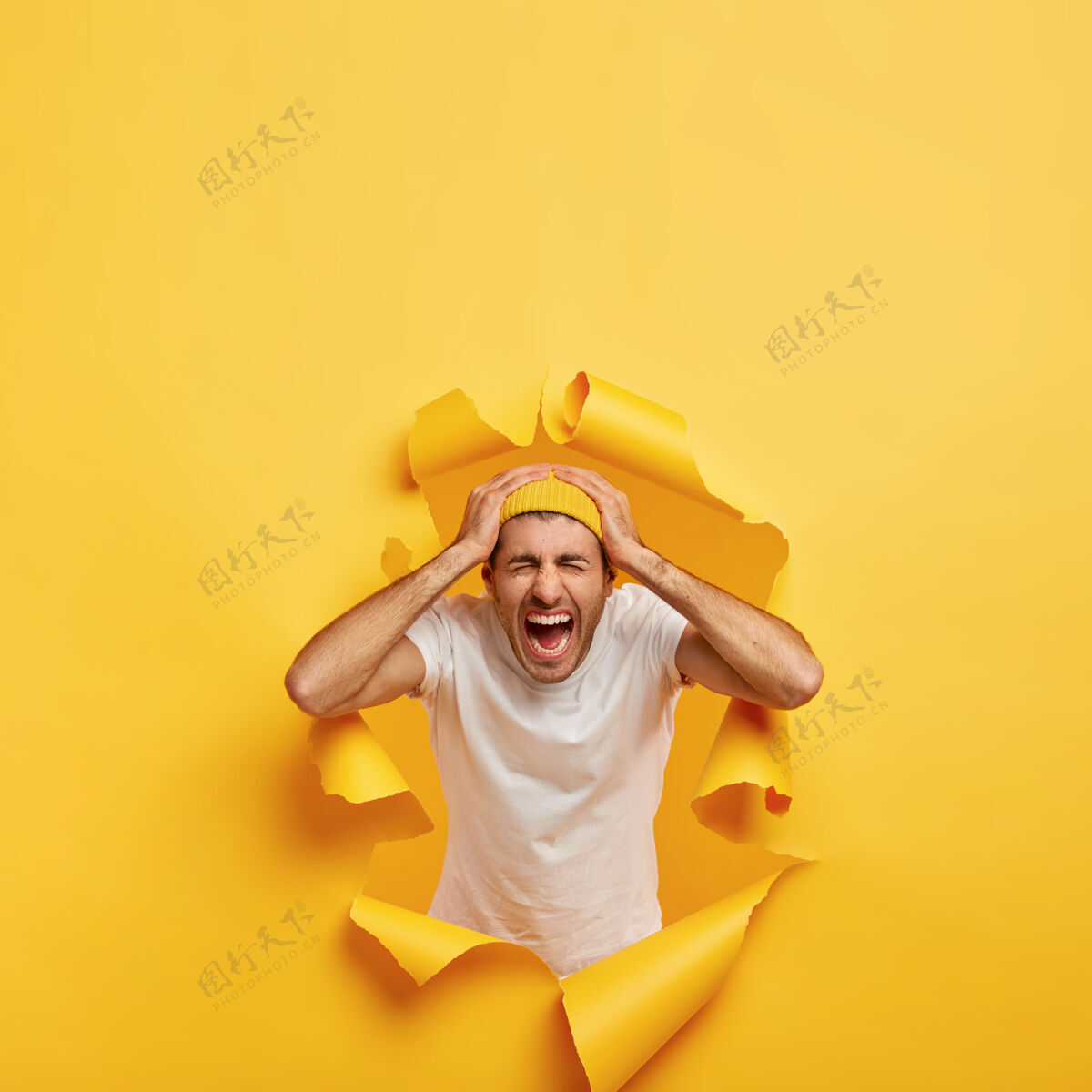 个人感性男生的垂直镜头双手触头 穿着休闲的白色t恤 时尚的黄色帽子姿势自由空间欧洲