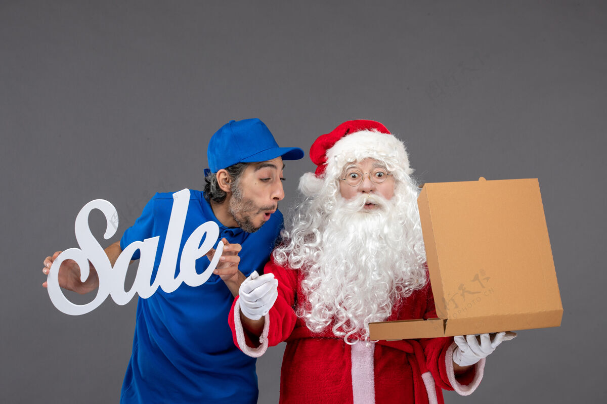人圣诞老人的正面图 男信使手持销售横幅 打开灰墙上的食品盒男圣诞快乐销售