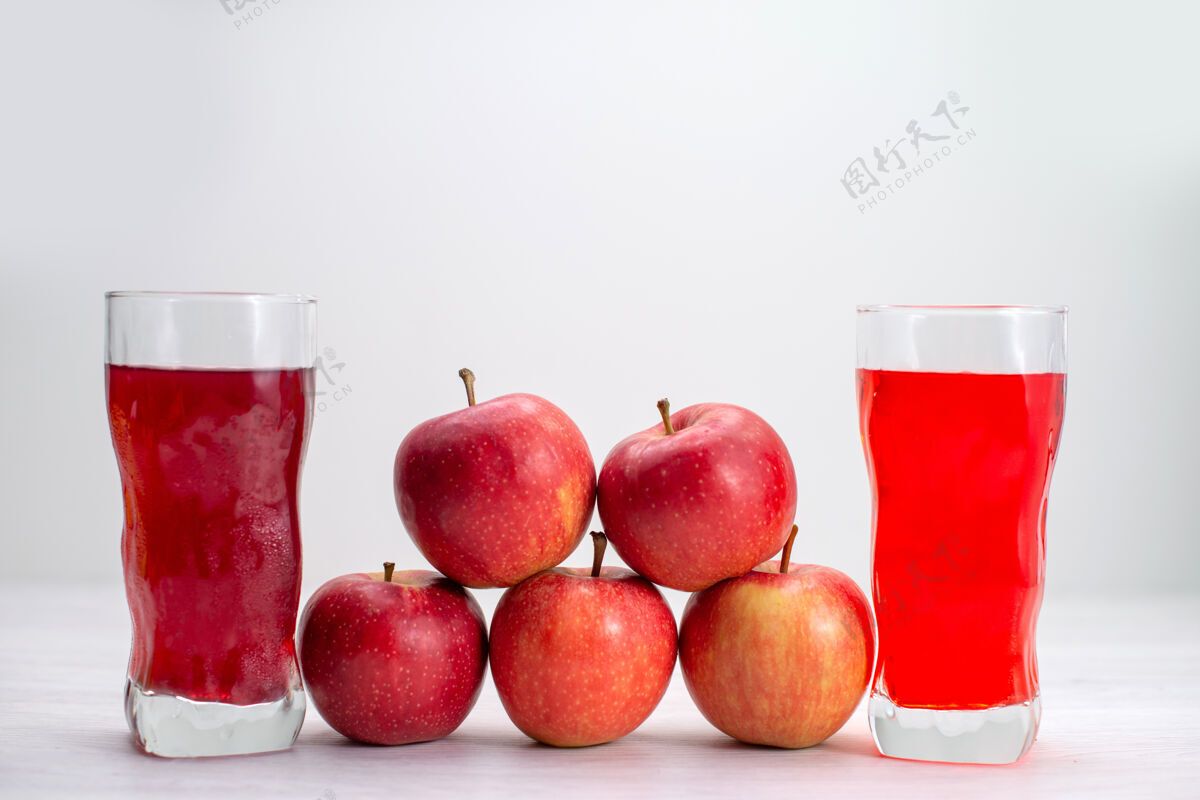 苹果正面图红色的新鲜苹果衬着白桌子上的果汁新鲜醇厚成熟的树上的植物果汁可食用的水果维生素