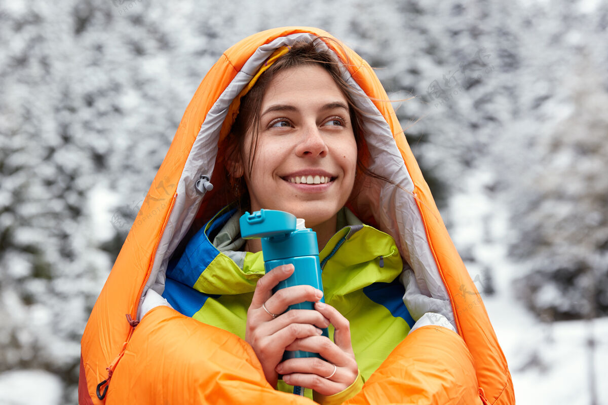 娱乐心满意足的欧洲女人戴着游泳袋 在雪山里旅行 手里拿着一瓶热饮高兴冷自然