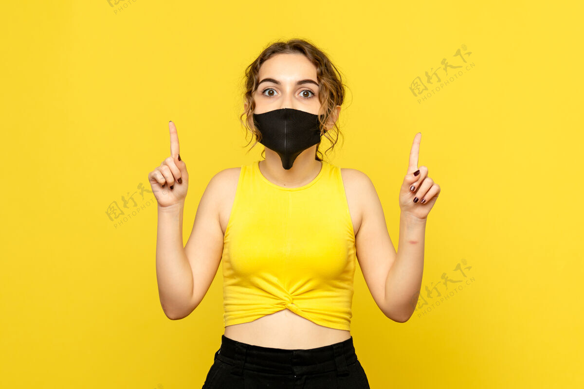 年轻女孩黄色墙壁上戴着黑色面具的年轻女孩的正视图成人防护人