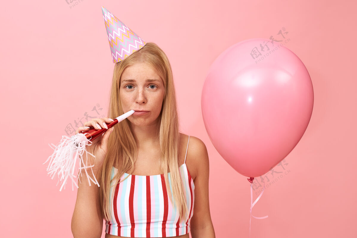 庆祝一幅孤独的肖像画：心烦意乱的年轻欧洲女性戴着圆锥形帽子和夏装庆祝生日 脸上露出心烦意乱的表情 吹着派对的号角氦成人女人