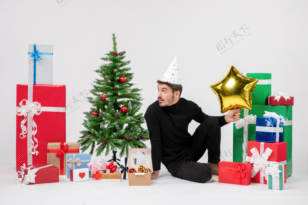 装饰年轻人围坐在礼物旁边 拿着金星在白墙上圣诞节前面礼物