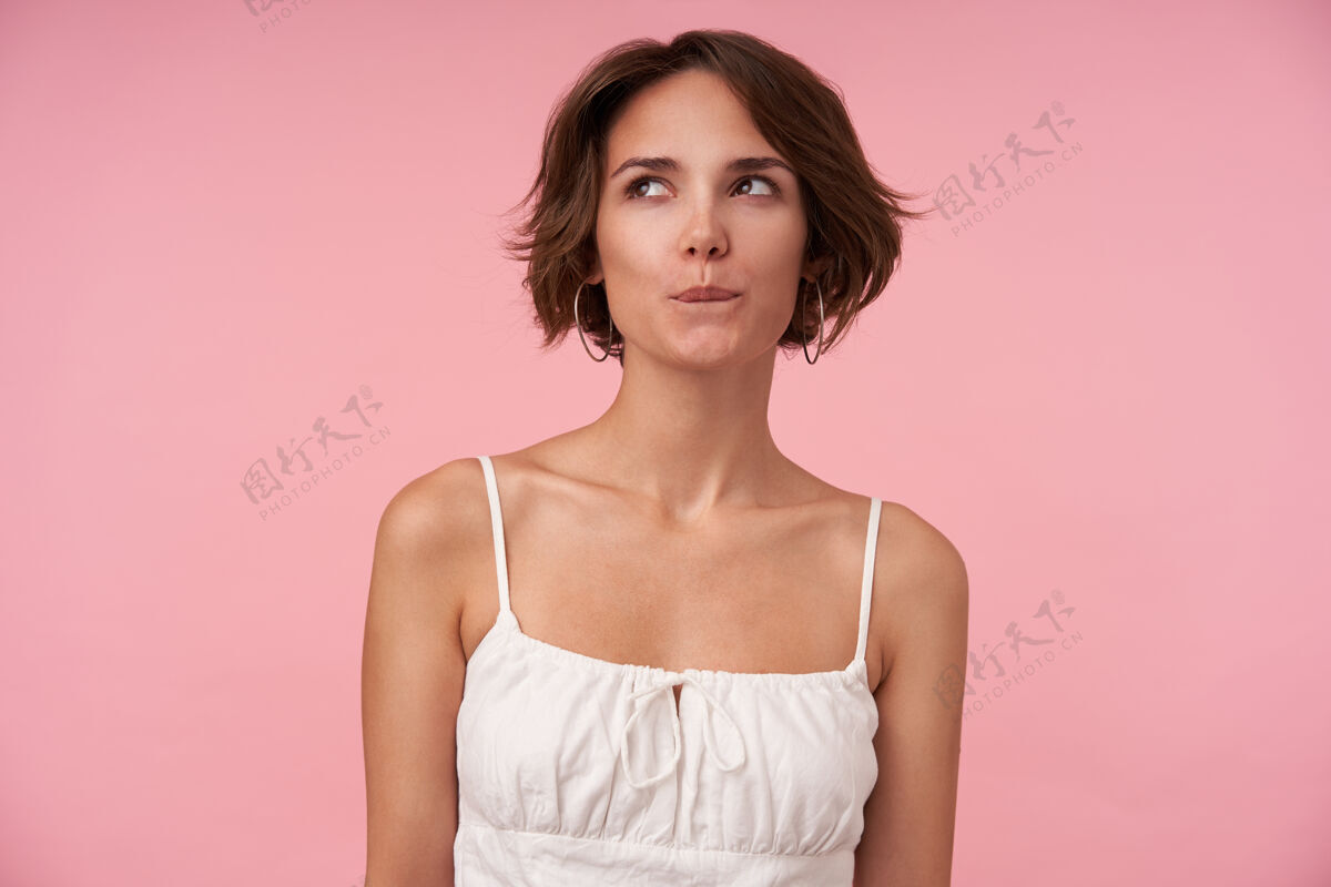 情绪一个留着休闲发型的年轻黑发女人的肖像 狡猾地向一边看 一边咬着内衣一边策划着什么 一边站着穿白色上衣摆姿势棕色女士
