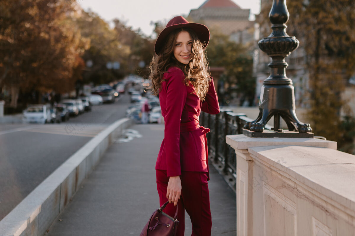 套装笑容可掬的时尚美女身着紫色西装行走在城市街头 春夏秋冬时节时尚潮流戴着帽子 手拿钱包深色阳光优雅