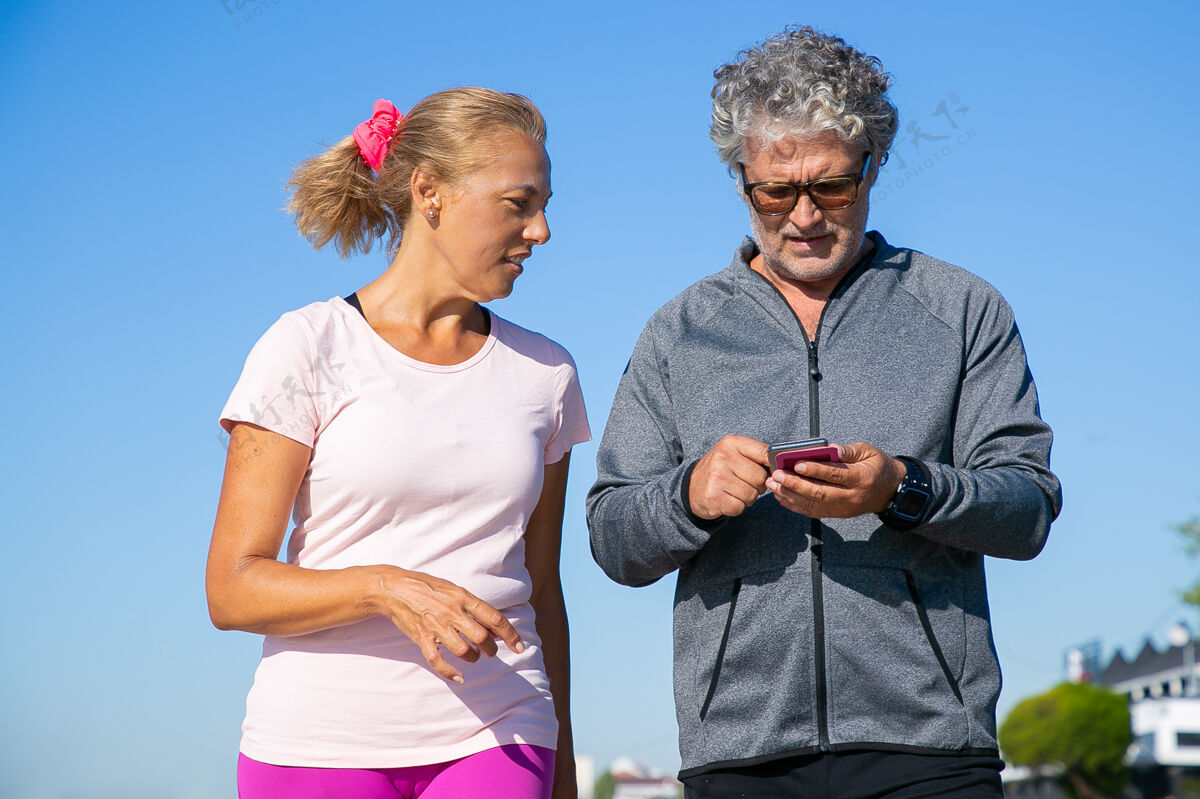 电话关注男性慢跑者在慢跑后使用手机上的健身应用程序成年夫妇穿着运动服 站在外面交流和运动概念的小工具活动跑步中等拍摄
