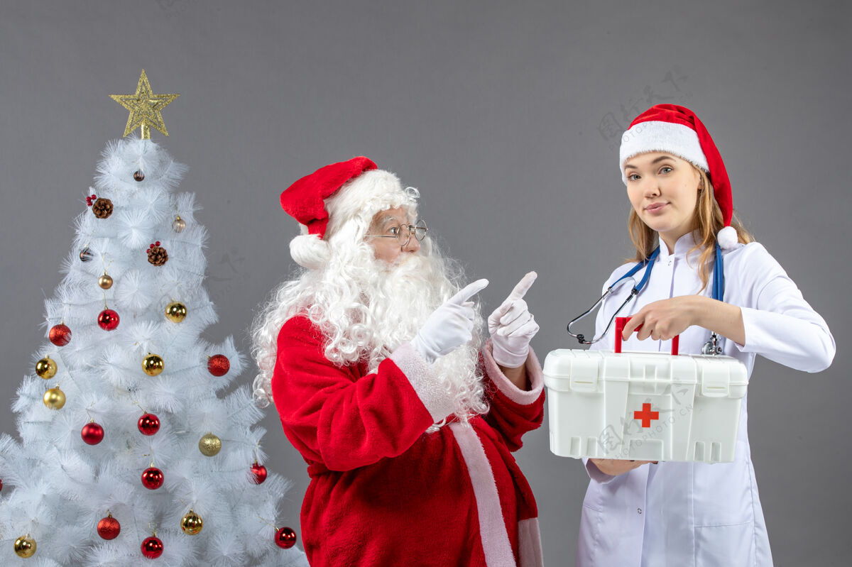 工具包圣诞老人和女医生的前视图 女医生拿着急救箱在灰色的墙上圣诞老人人们女性