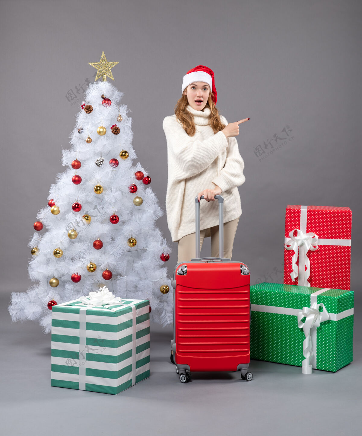 快乐前视图：拿着手提箱的女士展示了一些站在圣诞树和礼物旁边的东西快乐旅行站立