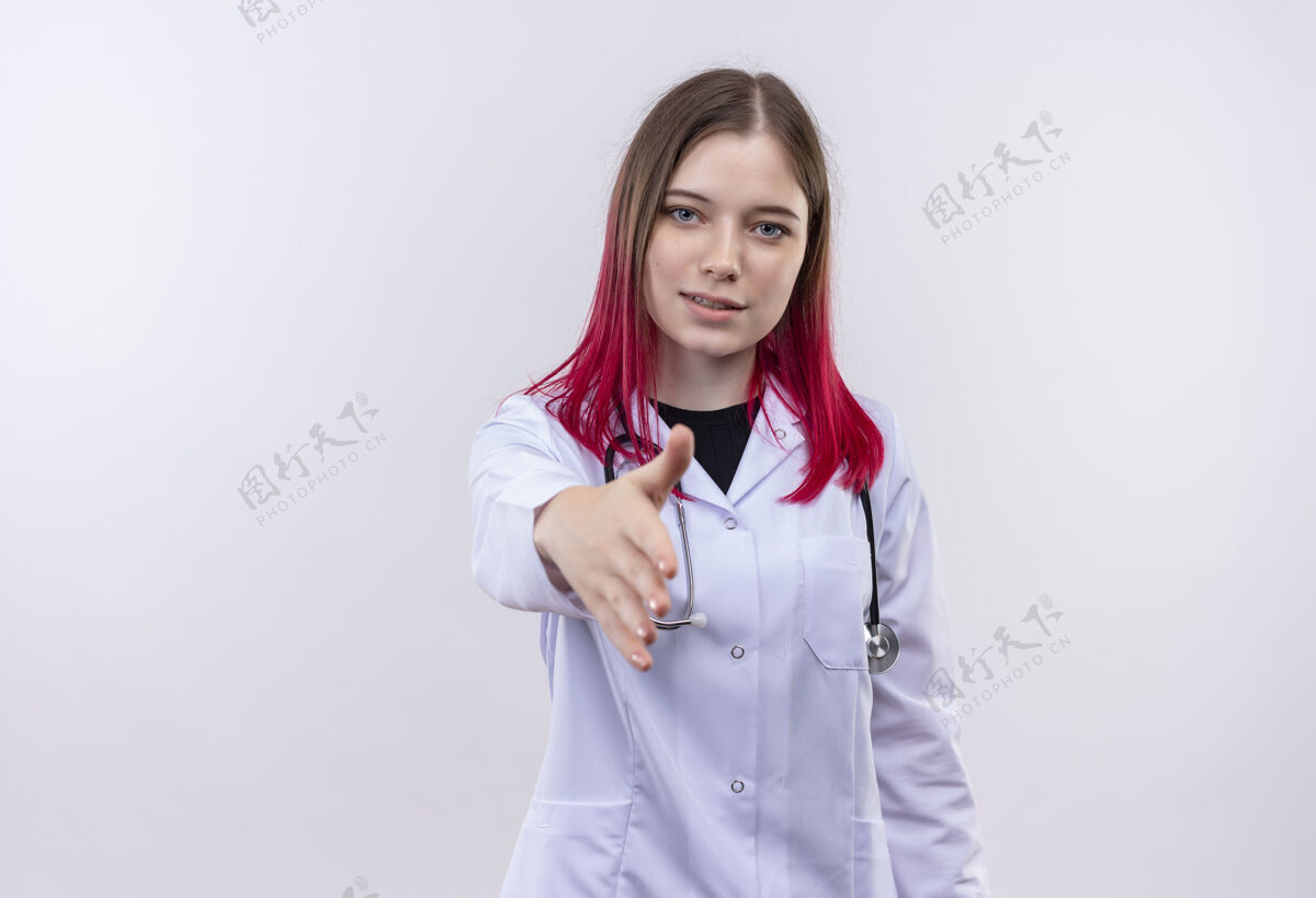 持有穿着听诊器医用长袍的年轻医生女孩高兴地在孤立的白色背景下向镜头伸出手来手白色医生