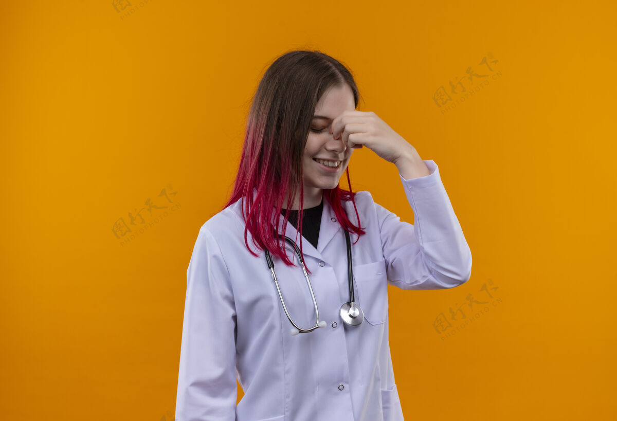 医生高兴的年轻医生女孩穿着听诊器医用长袍把手放在鼻子上孤立的橙色背景手橙色女孩