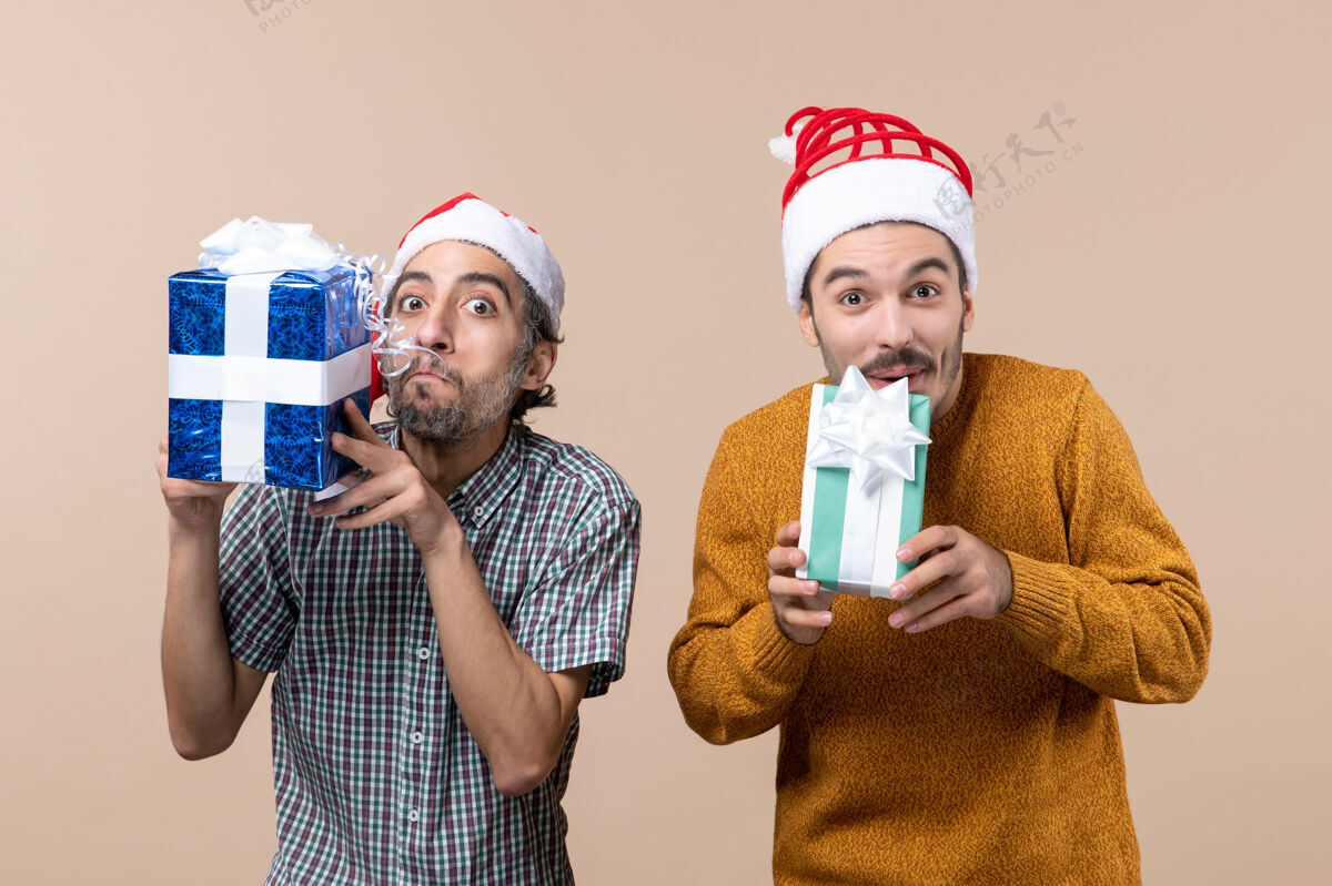 视图正面图两个戴着圣诞帽拿着礼物的快乐的家伙在孤立的背景下微笑脸前面