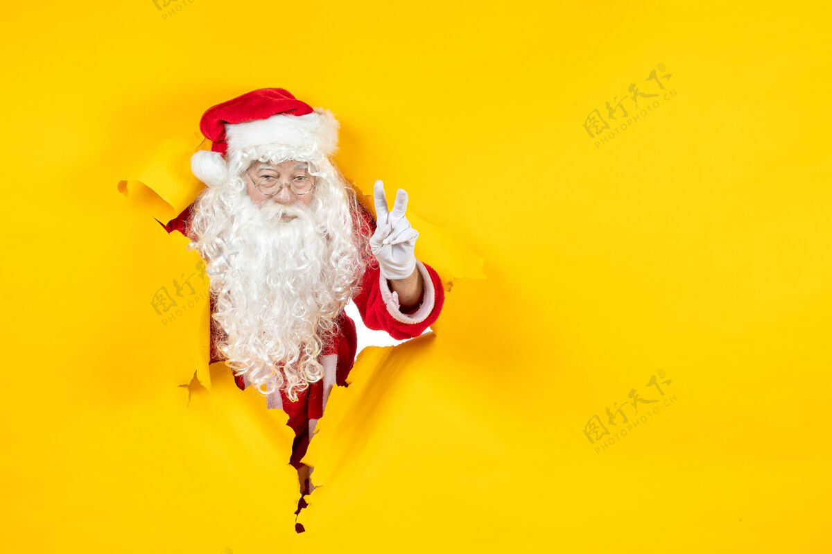 圣诞老人圣诞老人透过撕破的纸黄色墙壁看的正视图人人纸