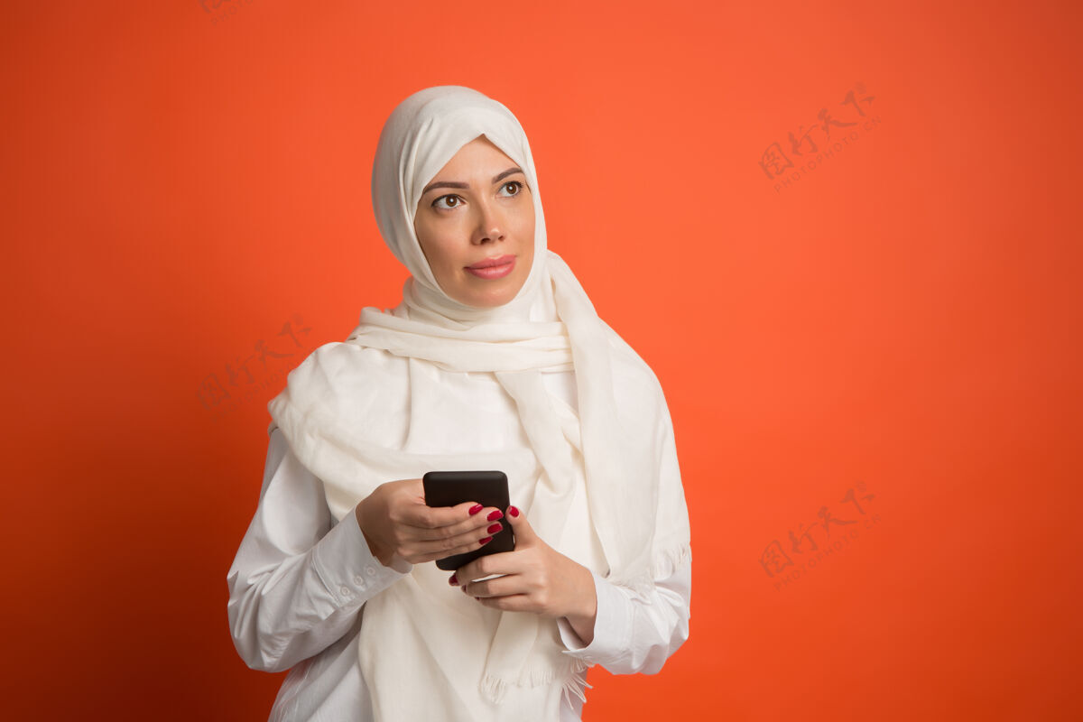 微笑戴着手机头巾的快乐阿拉伯女人微笑女孩的肖像 摆在红色工作室的背景下年轻感性的女人人类的情感 面部表情概念前视图表情穆斯林肖像