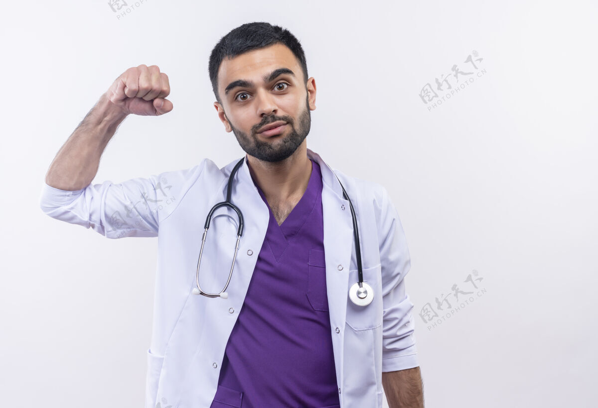 男性高兴的年轻男医生穿着听诊器医用长袍在孤立的白色背景上做着强烈的手势强壮白色医生