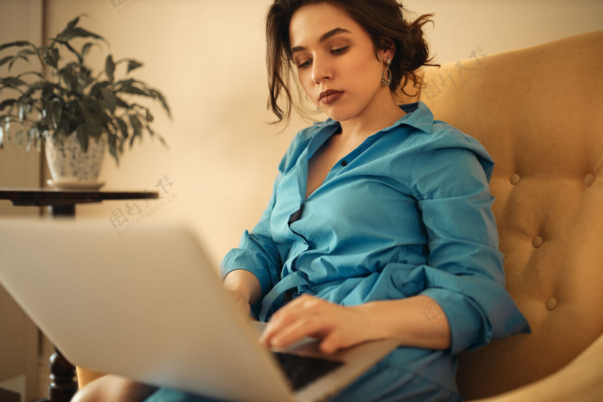 在线一位穿着蓝色连衣裙 坐在沙发上 膝上放着手提电脑的成功女商人科技女人职业