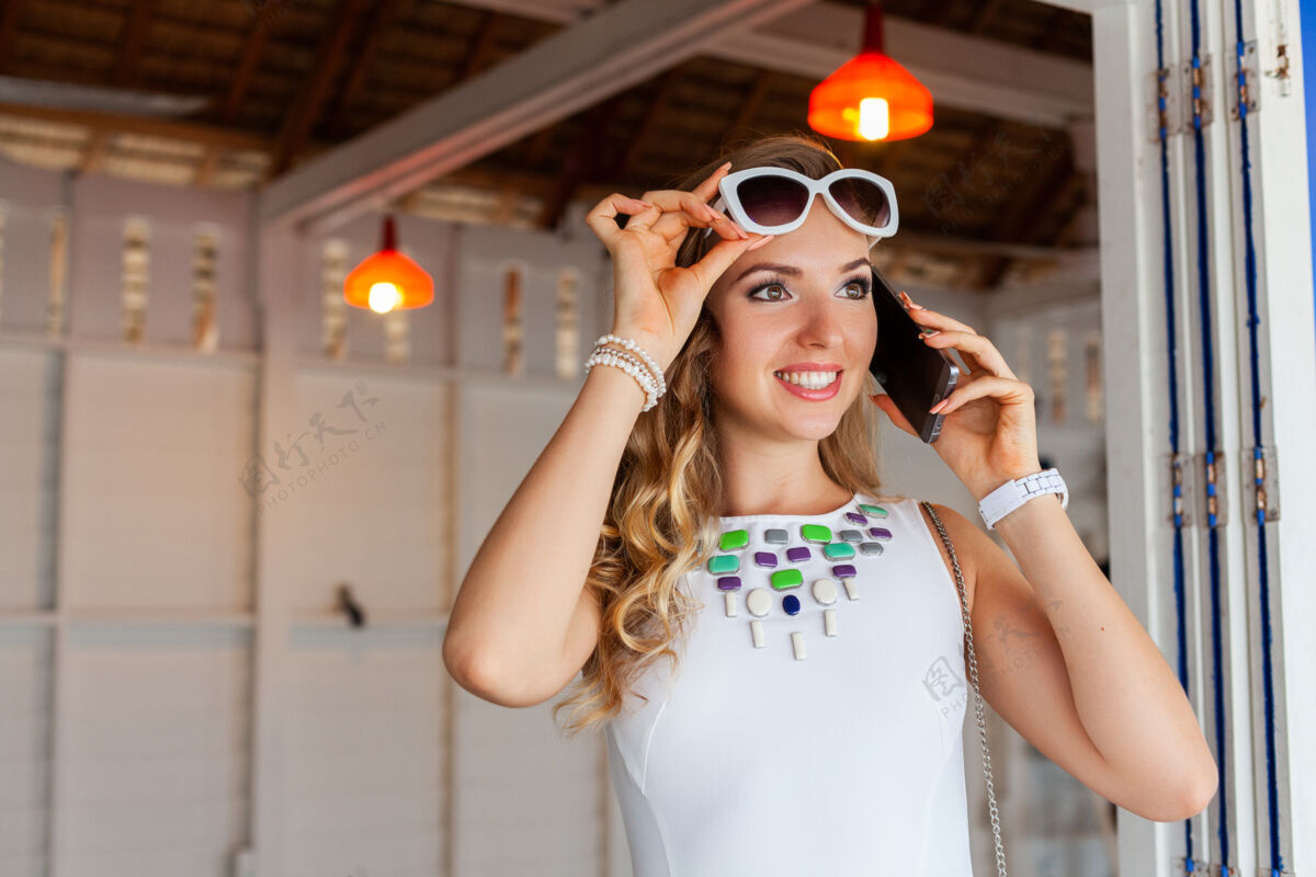 女性在夏日咖啡馆里 一个穿着白裙子 戴着墨镜的漂亮女人在打电话户外微笑漂亮