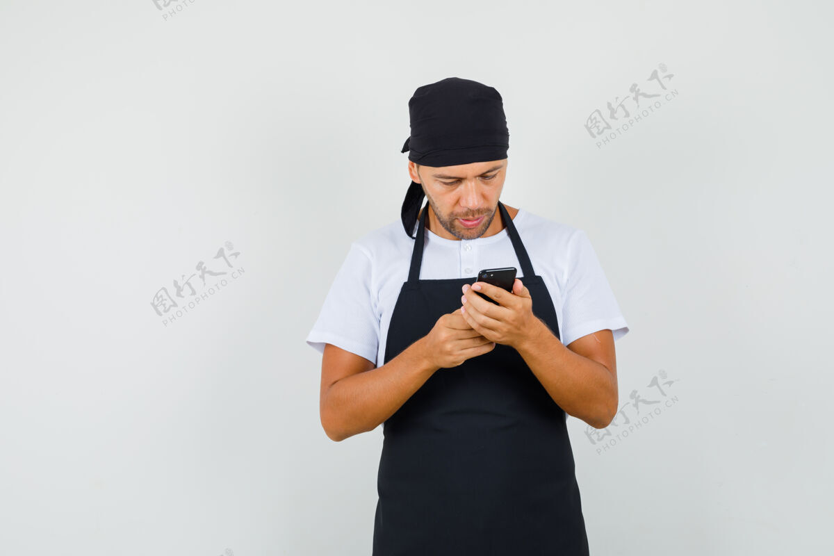 成人面包师穿着t恤 围裙 忙着用手机人食物挥手