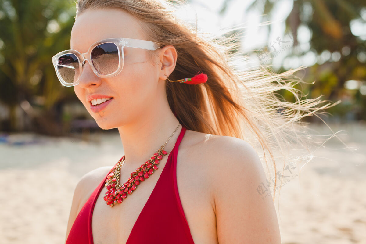 漂亮年轻漂亮的金发女人穿着红色泳衣 戴着太阳镜在沙滩上晒太阳头发女孩民族
