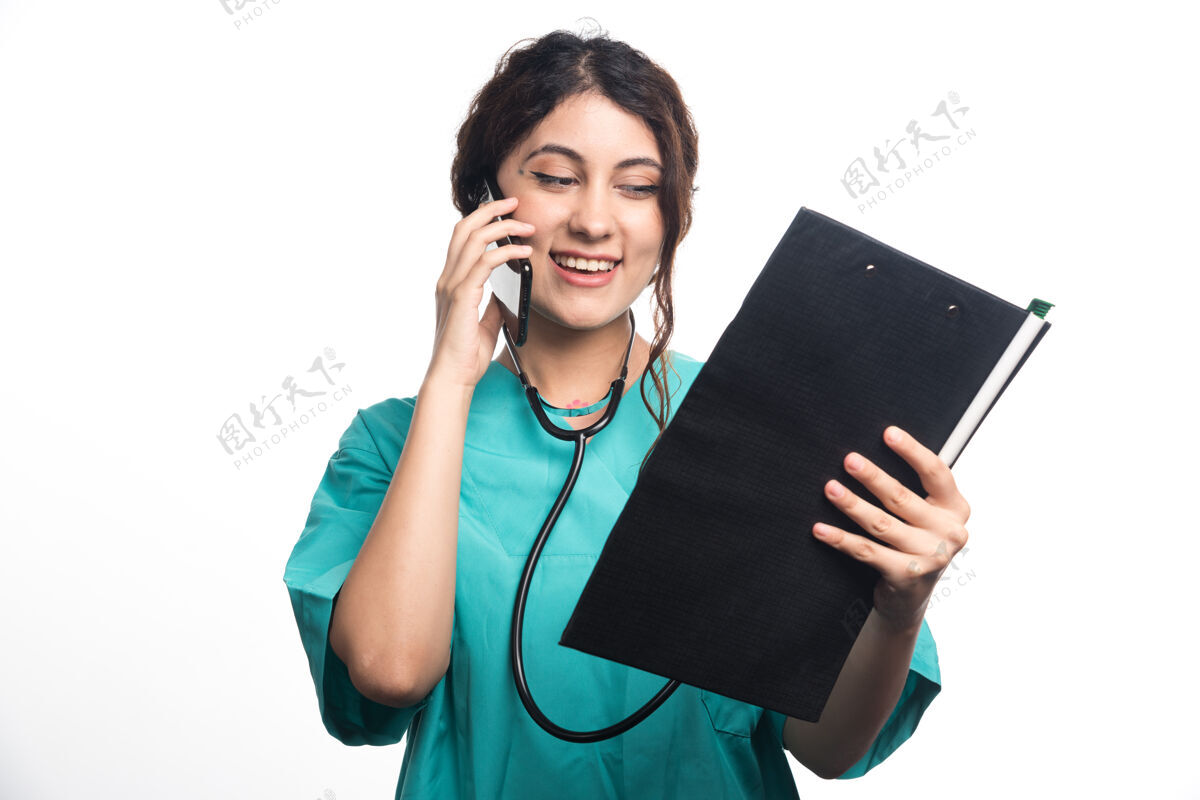 肖像年轻的女医生拿着剪贴板 在白色背景下讲着手机成人医生医生