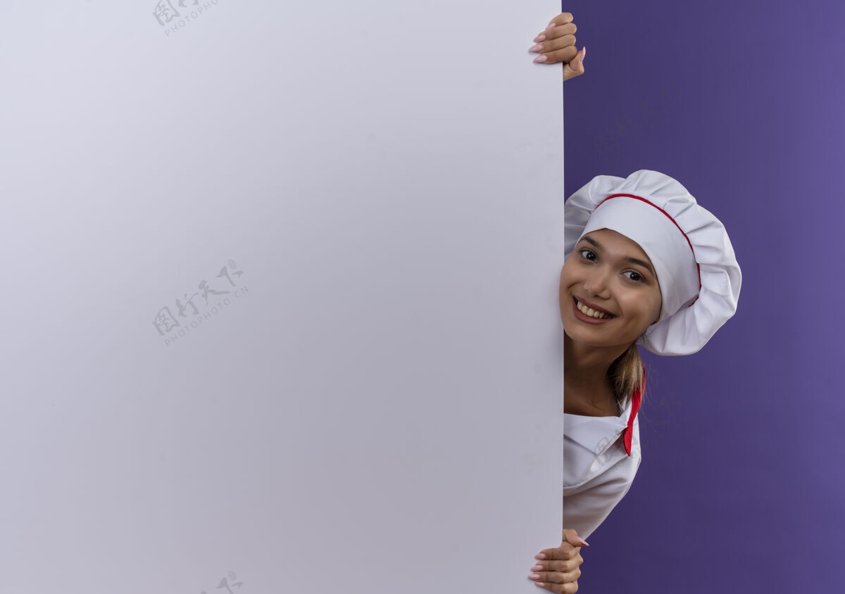 女微笑的年轻厨师女身穿厨师制服拿着白色墙壁在孤立的背景与复制空间戴着厨师厨师