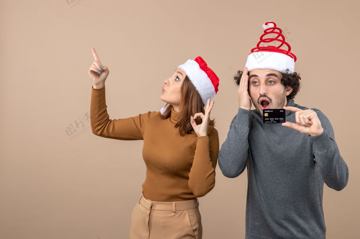 圣诞老人圣诞节心情激动迷茫酷酷情侣戴红色圣诞老人帽男人出示银行卡女人指着上面指向困惑红色