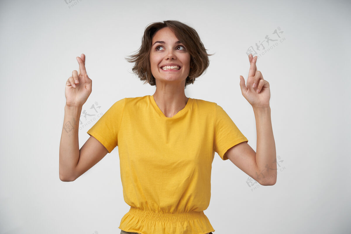 做梦快乐的年轻黑发女子 留着短发 双手交叉食指 积极乐观 希望自己的愿望成真 穿着黄色t恤摆姿势黑发美丽棕色