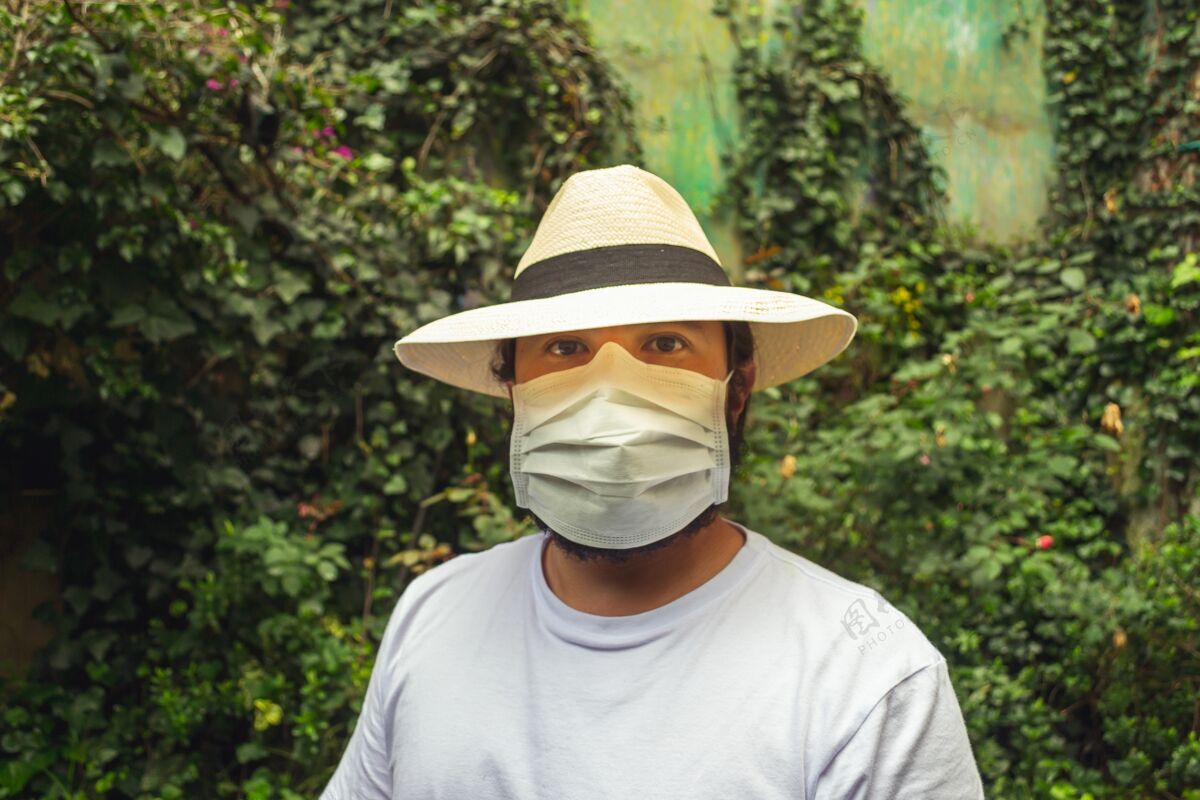 疾病戴着白色口罩戴着帽子的男人在花园里防止灰尘和冠状病毒疾病灰尘冠状病毒