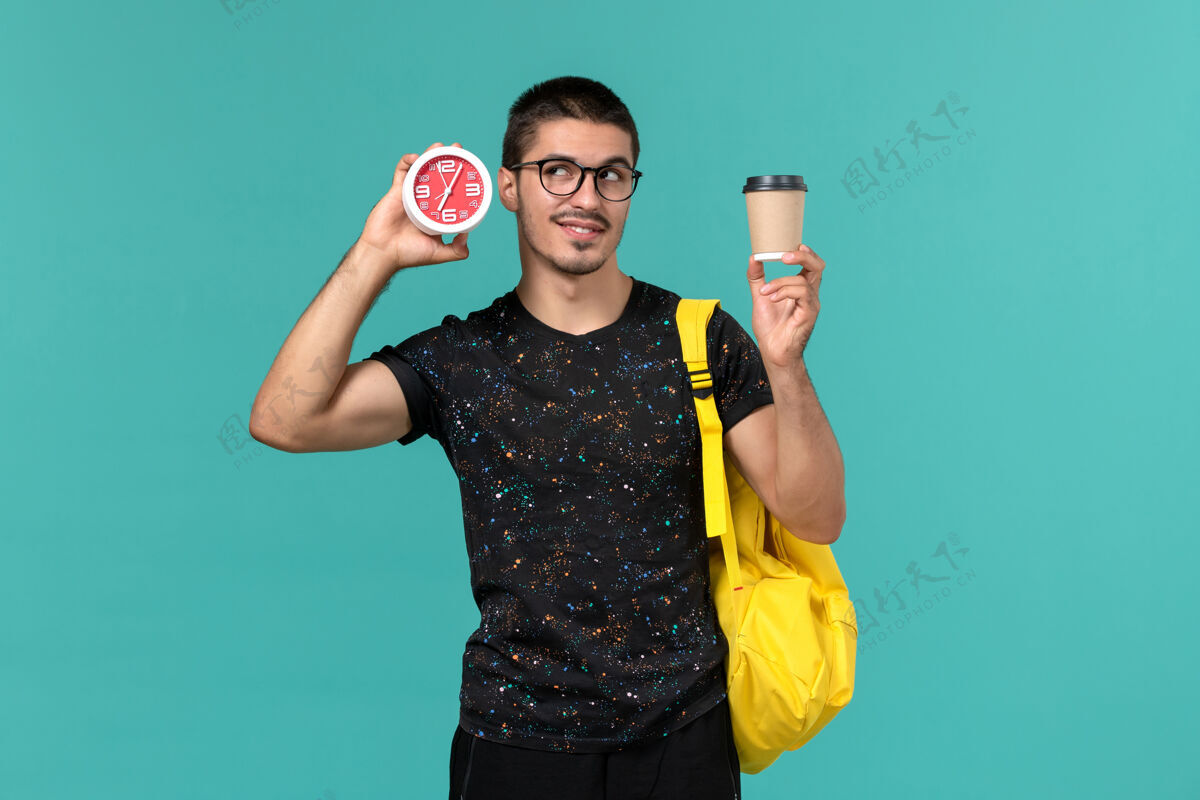 肖像身穿深色t恤的男生正面图黄色背包 蓝色墙上放着咖啡和时钟学生大学咖啡