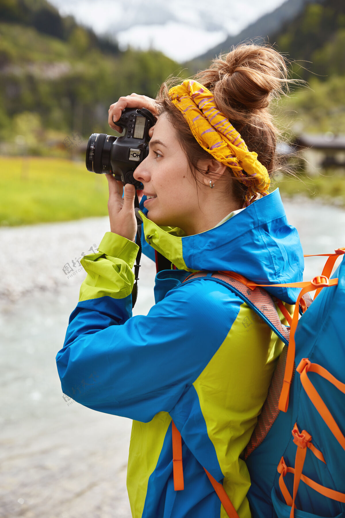 设备流浪女走在山间的绿色草地上 用数码相机拍摄精彩的照片 欣赏大自然的美景 穿着夹克草地爱好摄影师
