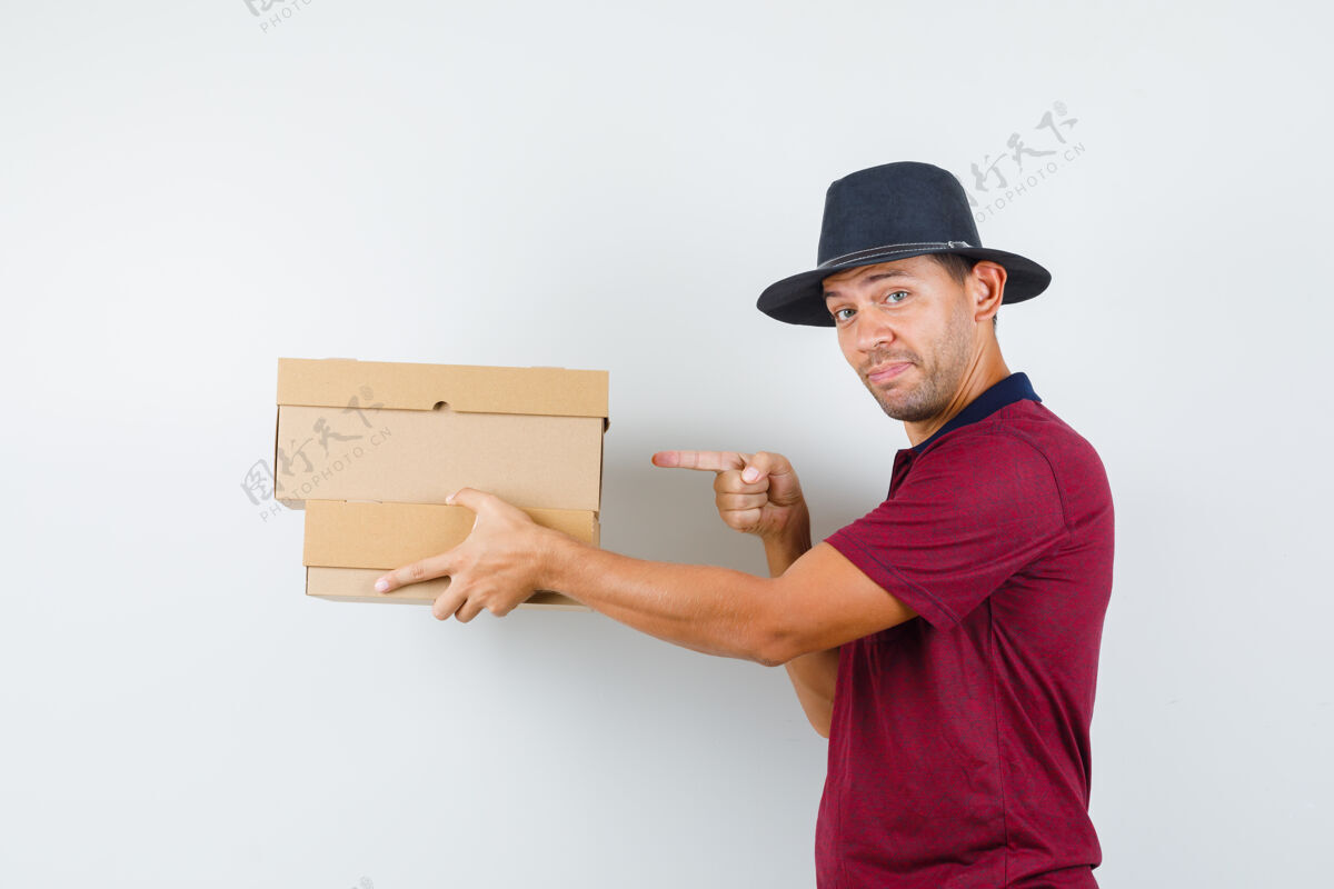 年轻一个穿着红衬衫 戴着黑帽子的年轻男人 一边拿着盒子一边指着盒子表情看英俊