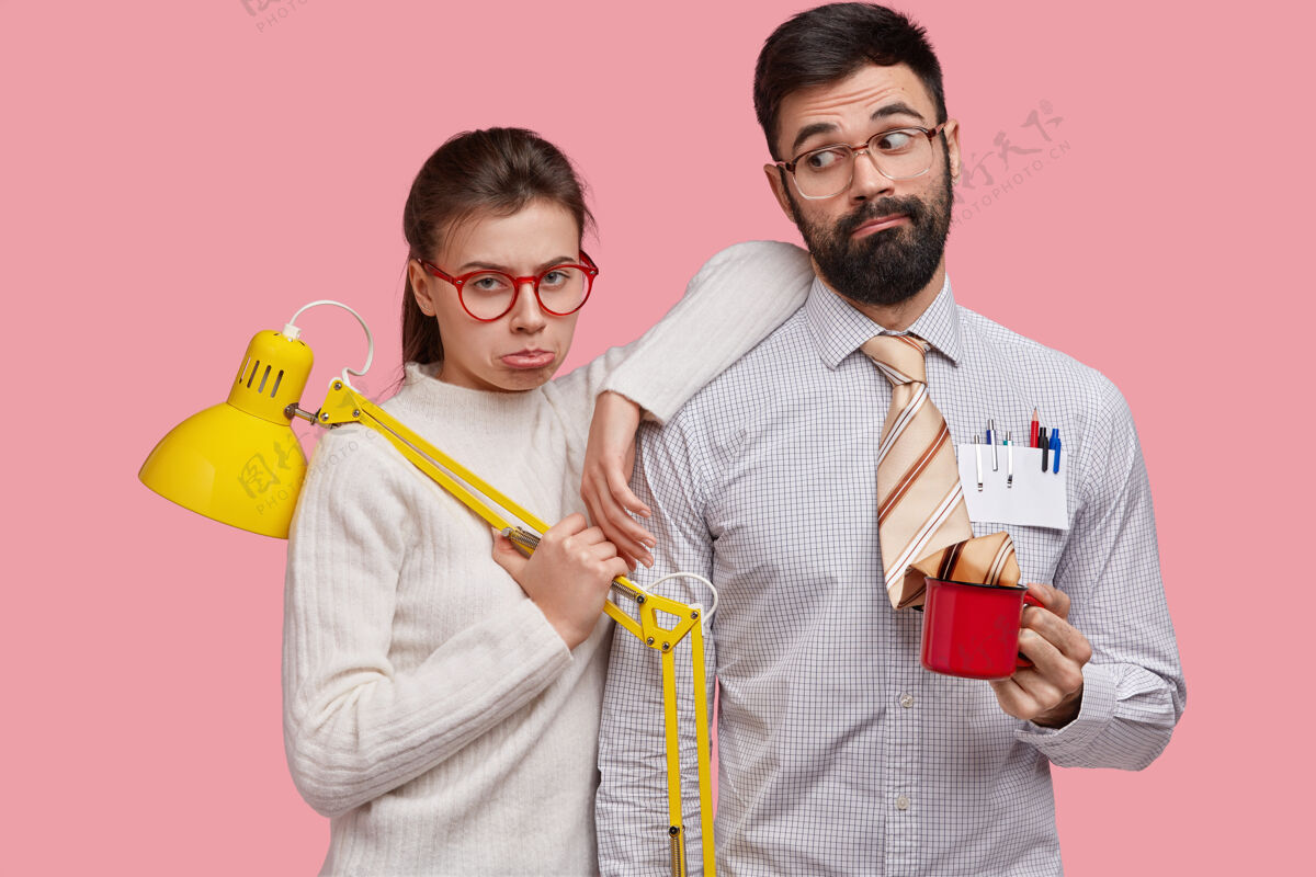 眼镜伤心不高兴的戴眼镜的女人和男人 做共同的工作 拿着台灯和咖啡杯 表达消极的情绪同事呆子杯子