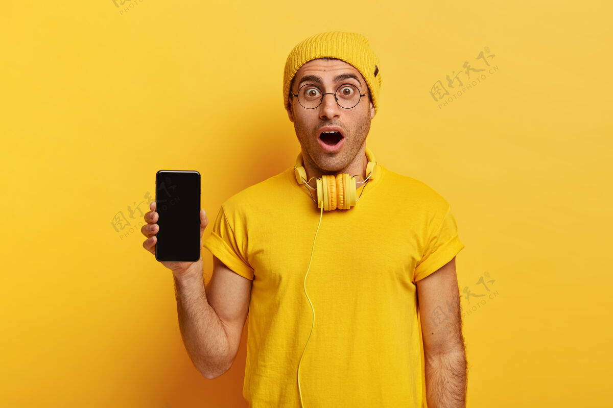 震惊照片中惊讶的家伙拿着空屏幕的现代手机 从震惊中张嘴智能手机剃胡子麻木
