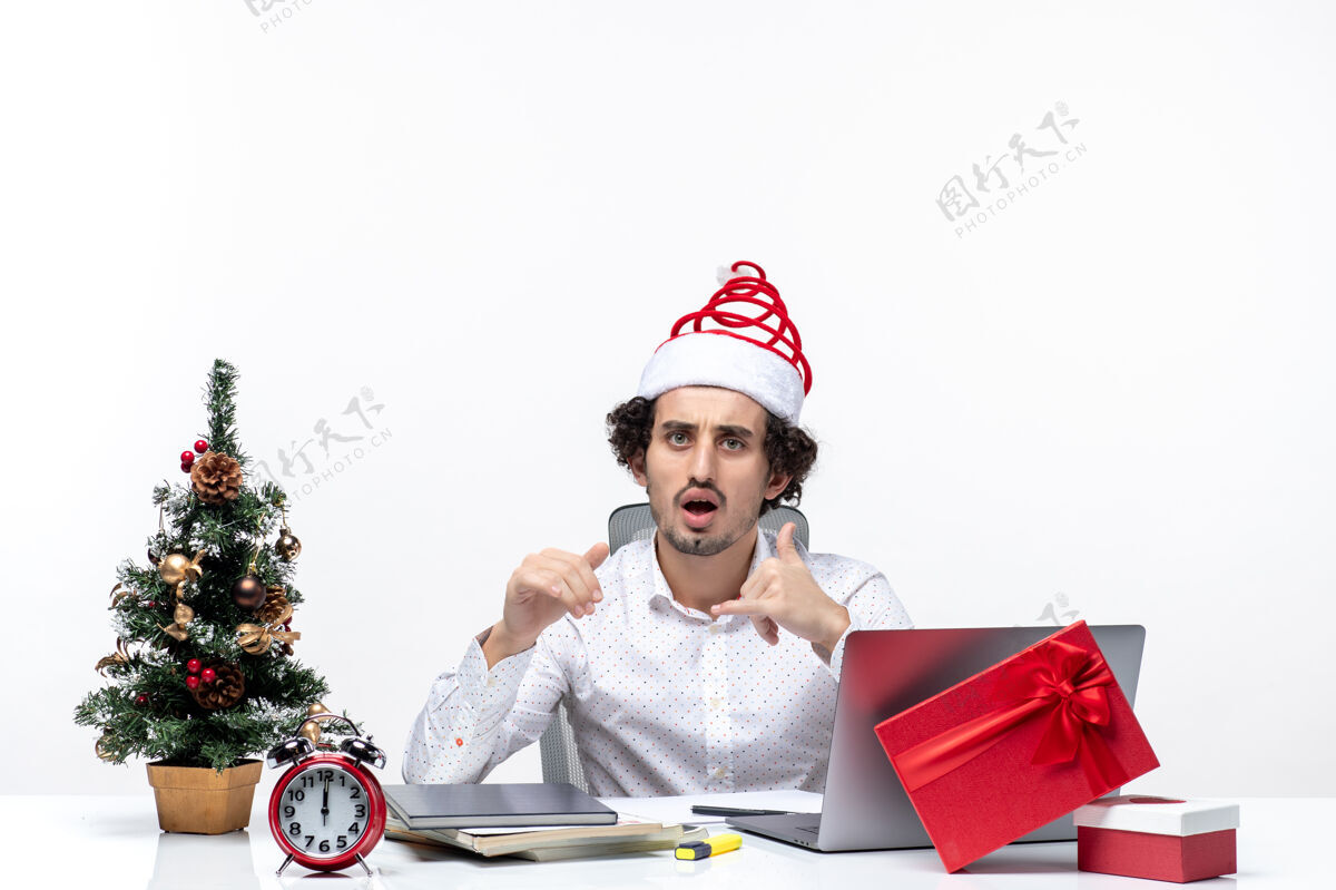 生活震惊的年轻商人与有趣的圣诞老人帽子和庆祝圣诞节在白色背景的办公室圣诞老人人庆祝