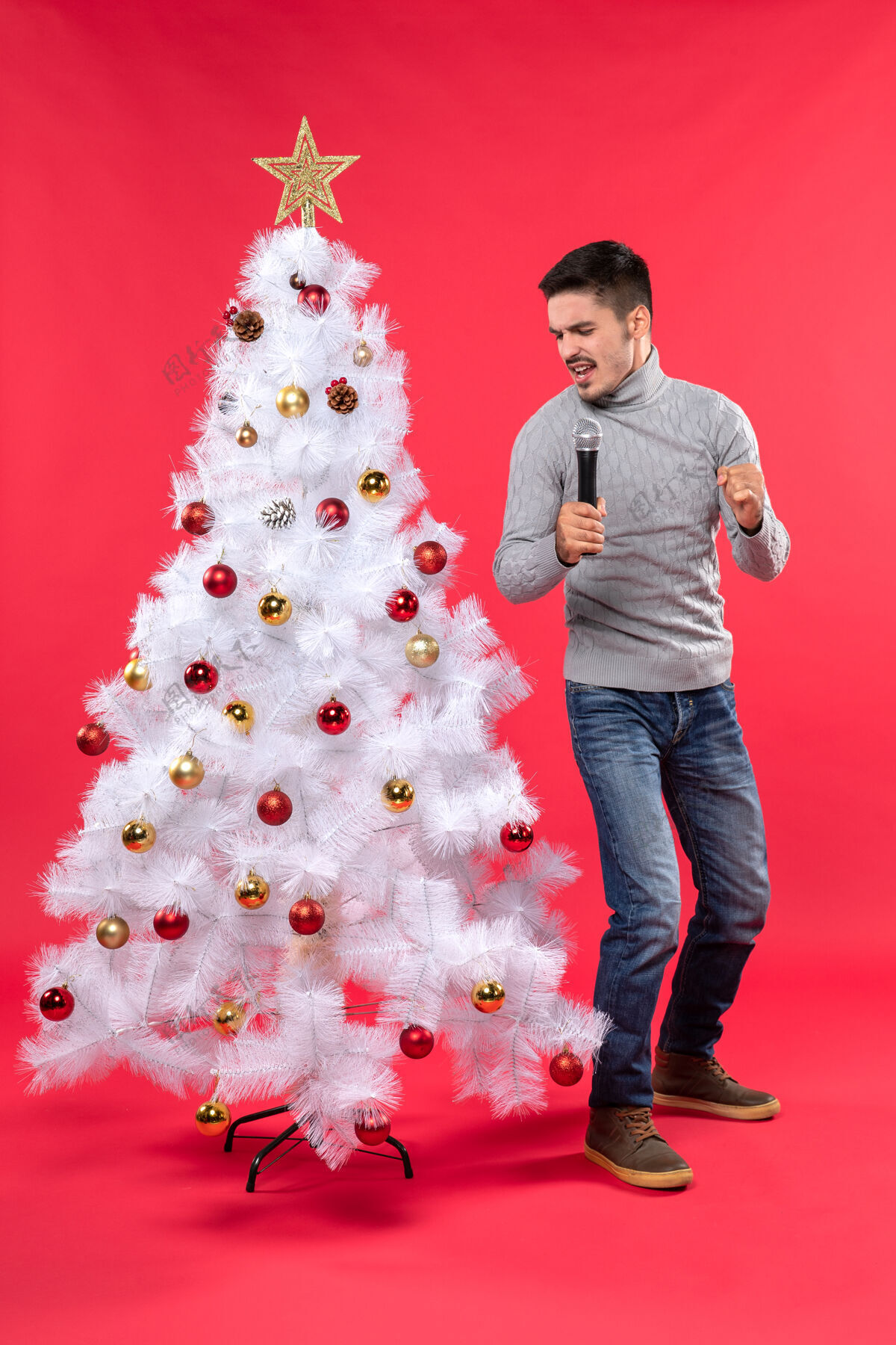 快乐圣诞节的心情与自信的家伙穿着牛仔裤站在装饰圣诞树附近 手持麦克风唱歌衣服自信站着