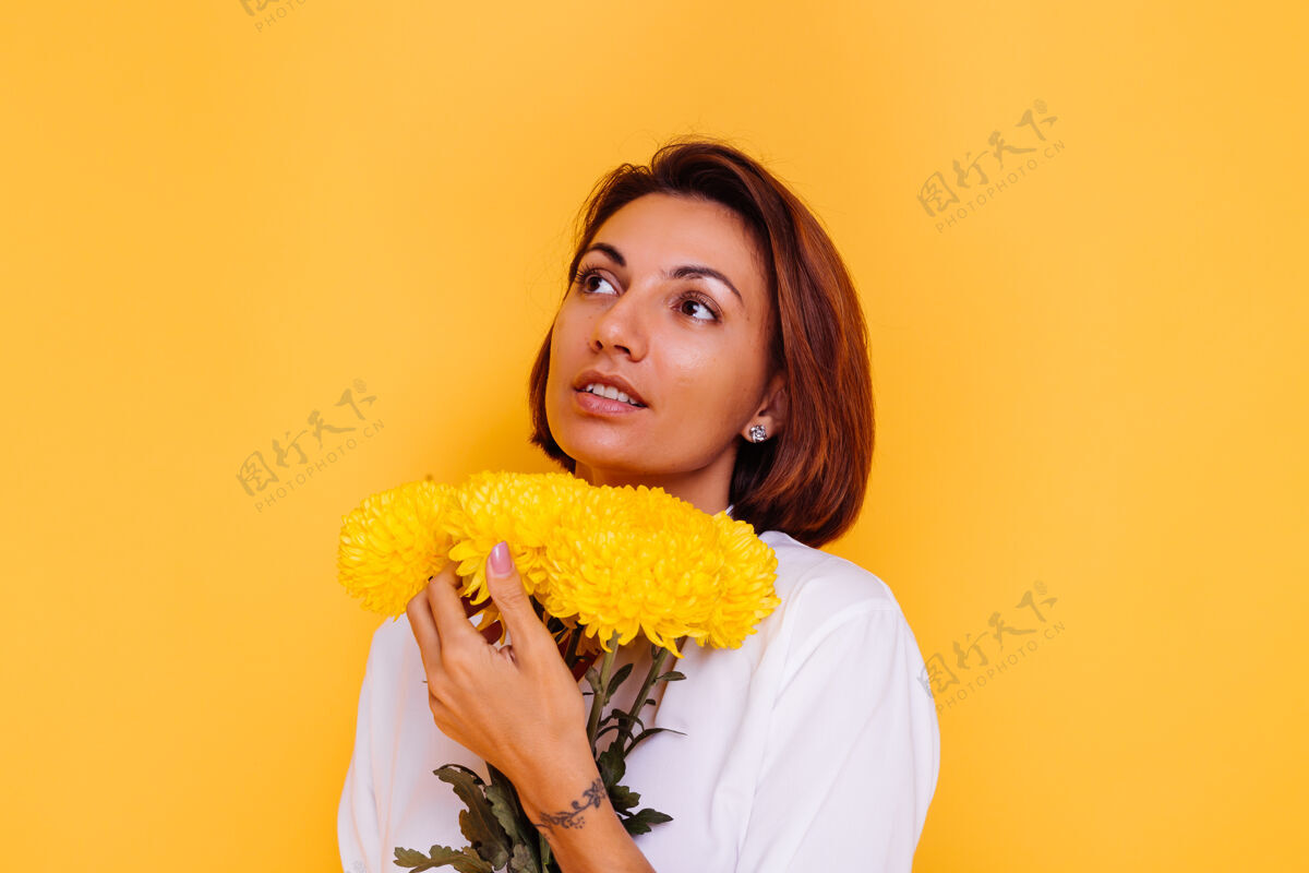 气味摄影棚拍摄的黄色背景快乐的白人妇女短发穿着休闲服白衬衫和牛仔裤手持一束黄色紫苑积极快乐惊喜