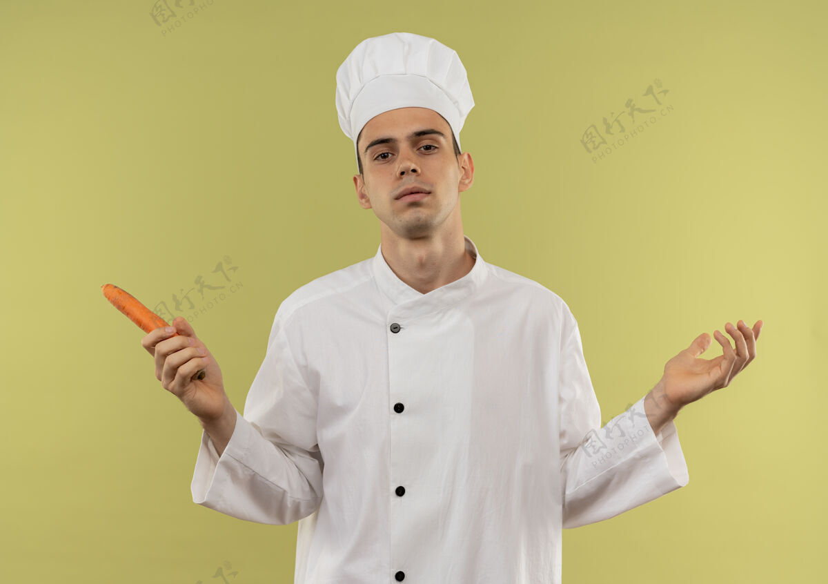 制服自信的年轻男厨师穿着厨师制服 手里拿着胡萝卜 在与世隔绝的绿墙上摊开双手手厨师厨师