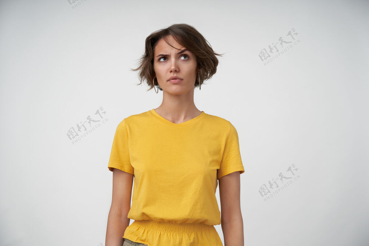 肖像迷惑不解的年轻黑发女子 穿着黄色t恤 手朝下摆姿势 扬起眉毛向上看眉毛女性20多岁