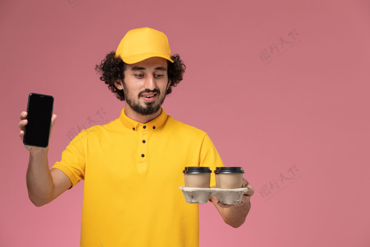 工作正面图：身穿黄色制服的男信使手拿棕色咖啡杯 粉色墙上挂着电话信使送货视野