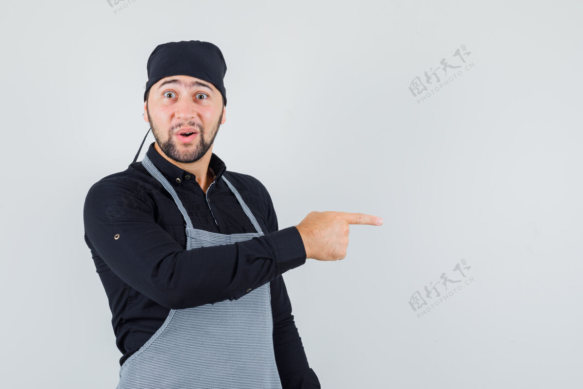 烹饪男厨师穿着衬衫 围裙指向一边 看上去很惊讶 正面视图烹饪食物制服