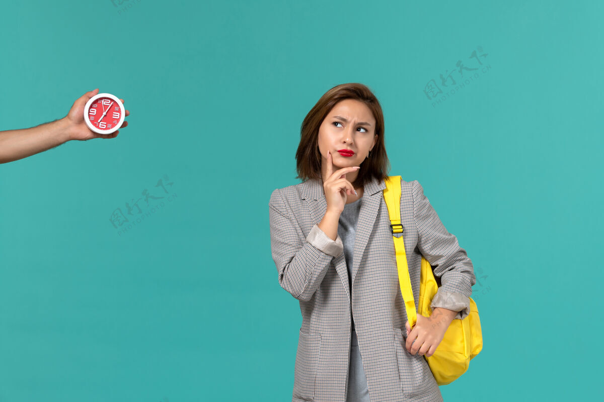Female身穿灰色夹克 背着黄色背包的女学生在浅蓝色墙上思考的正面图穿戴学校气球
