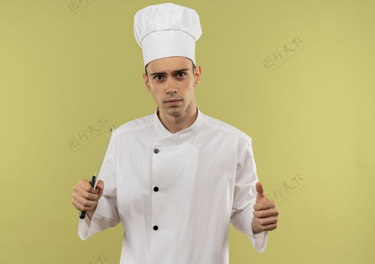 菜刀自信的年轻男厨师穿着厨师制服 手拿菜刀 大拇指竖立在隔离的绿色墙壁上 留有复印空间男性抱着厨师