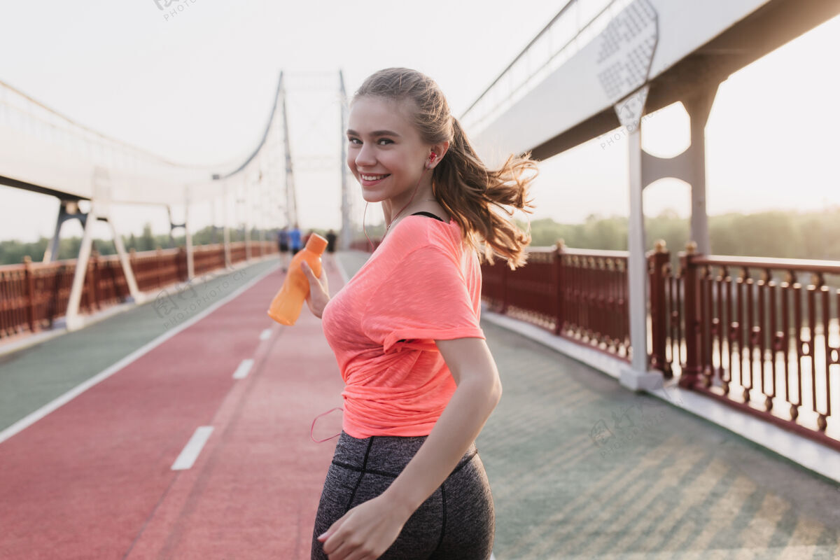 女性从后面的肖像壮观的白人女孩运行与瓶水快乐的女跑步者在粉红色的t恤衫看肩人动作跑步者