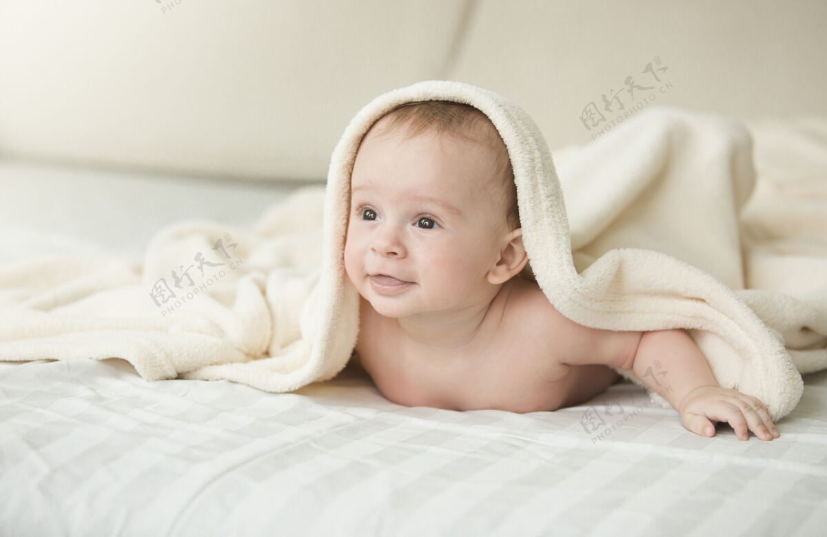 男性可爱快乐的婴儿躺在床上的毯子下的画像婴儿阳光放松